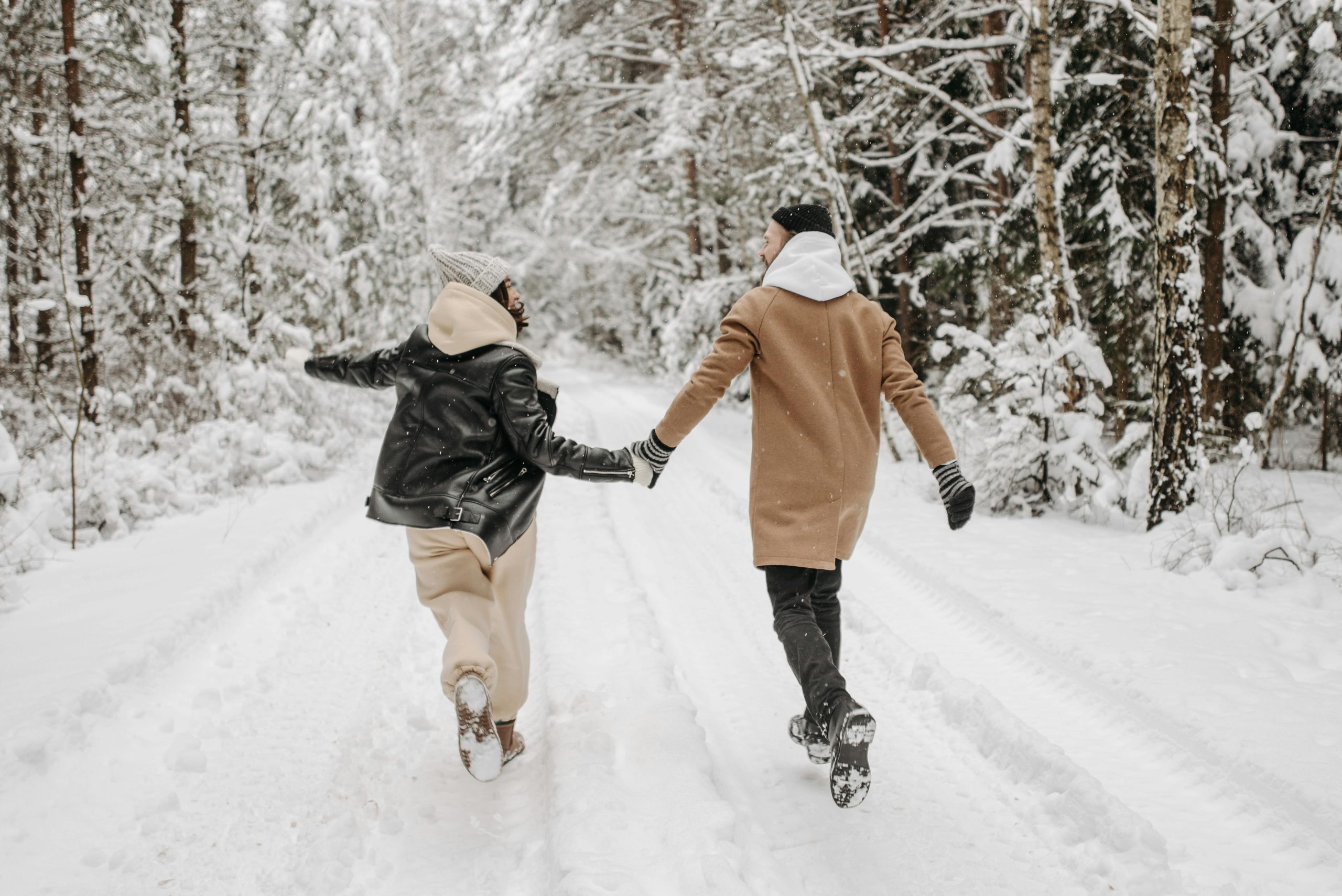 Playful couple holding hands while running through a snowy forest trail